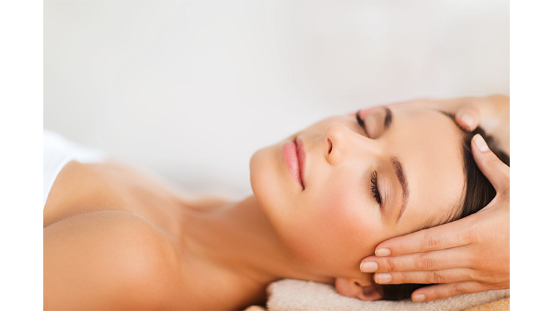 Close-up of a woman with closed eyes receiving a facial massage.
